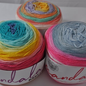 May include: Three colorful yarn balls in shades of pink, yellow, blue, and green. The yarn is arranged in a circular pattern, with each ball displaying a gradient of colors. The yarn is labeled "Mandala Baby".