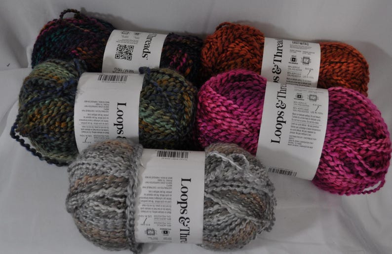 May include: Five skeins of Loops & Threads yarn in various colours including dark purple, orange, green and blue variegated, bright pink, and grey with brown flecks. Each skein features a white paper label with brand text and product information.
