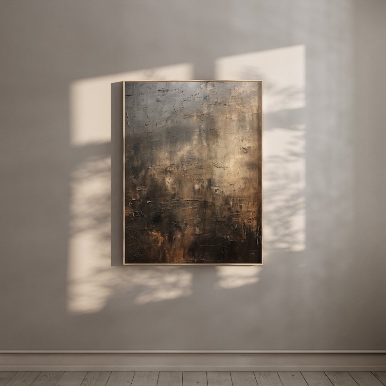 May include: Abstract painting in shades of brown, gold, and black with a textured surface. The painting is framed in a thin, light wood frame and is hanging on a light beige wall.