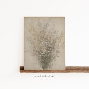 May include: Abstract art print featuring a textured background with a cluster of light brown and green shapes resembling a bouquet of flowers. The print is framed and displayed on a wooden shelf. The text "Eine Art Liebe" is printed below the image.
