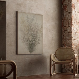 May include: A light brown wicker chair with a woven back and seat sits in a room with a textured wall. A framed abstract painting with a light gray background and green and white accents hangs on the wall.