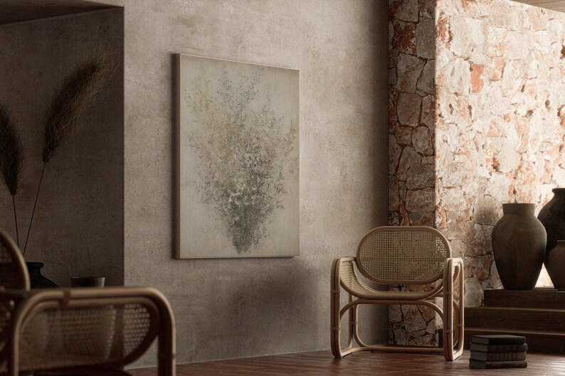 May include: A light brown wicker chair with a woven back and seat sits in a room with a textured wall. A framed abstract painting with a light gray background and green and white accents hangs on the wall.