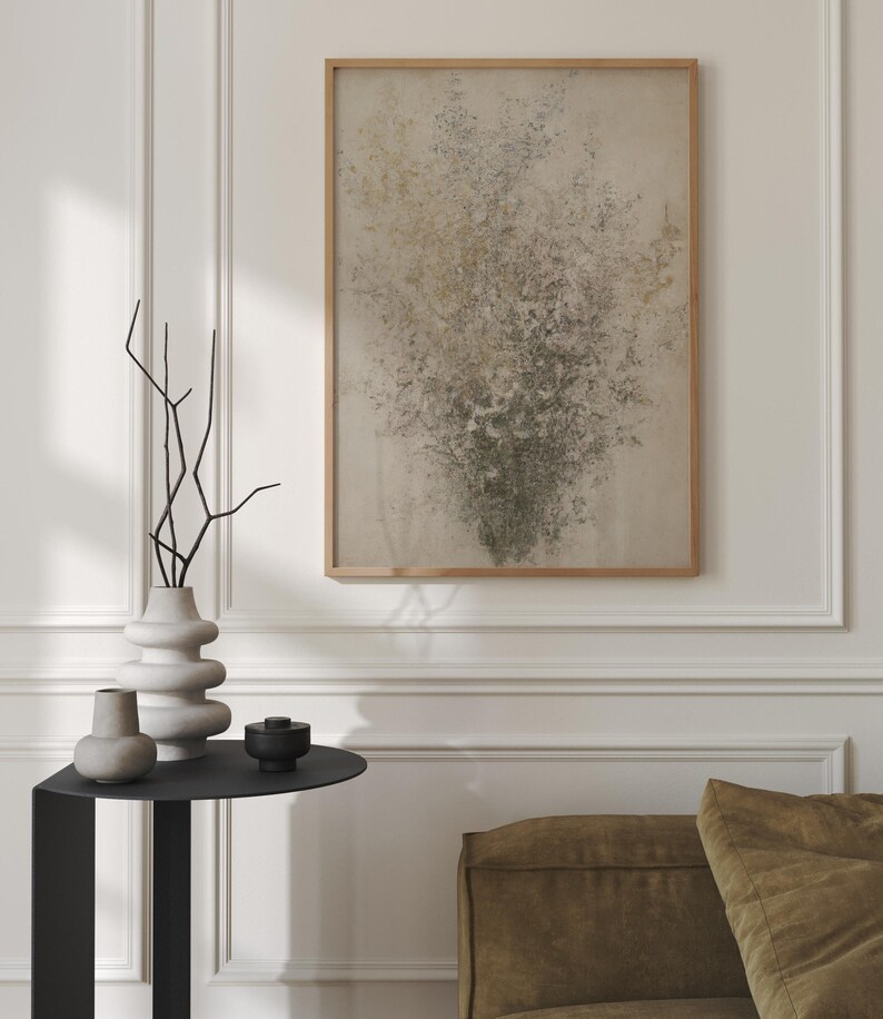 May include: A black side table with a round top and a vase with dried branches, a smaller vase, and a small black bowl. A framed abstract painting with a beige background and green and brown accents hangs on the wall behind the table. A brown couch is in the background.