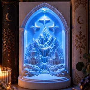 Könnte beinhalten: Eine weiße, bogenförmige 3D-gedruckte Diorama-Lampe mit einer detaillierten Bergkette, einem zentralen Wasserfall und Schlossstrukturen. Die Szene wird durch ein hellblaues LED-Licht beleuchtet, mit drei in den oberen Bogen geschnitzten Sternen.