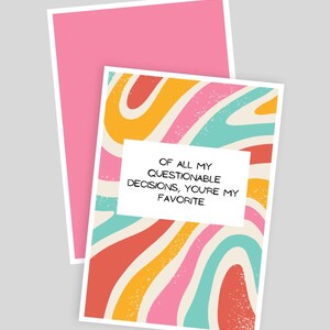 Op de afbeelding: Een rechthoekige wenskaart met een golvend, veelkleurig patroon van roze, oranje, turquoise en crème. Een wit rechthoekig kader in het midden bevat de zwarte tekst: OF ALL MY QUESTIONABLE DECISIONS, YOU'RE MY FAVORITE. Een roze envelop ligt erachter.