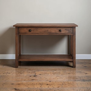 Puede incluir: Una mesa consola rectangular de madera con un acabado marrón medio. La mesa cuenta con un único cajón horizontal situado justo debajo de la superficie superior, equipado con dos pequeños pomos circulares oscuros. Tiene cuatro patas rectas.