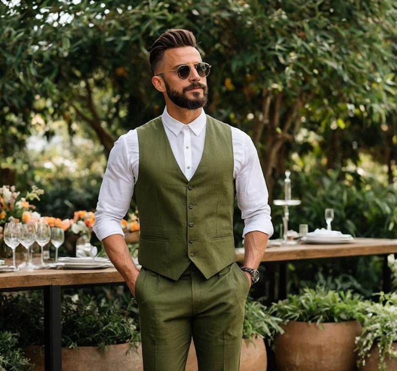 May include: A man wearing a green vest and matching pants with a white button-down shirt. He is wearing sunglasses and has a beard.