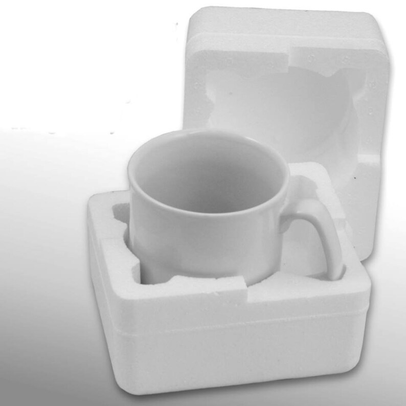 Pode incluir: Uma caneca de caf&eacute; de cer&acirc;mica branca com uma al&ccedil;a curva, colocada em uma embalagem protetora de espuma branca. A caneca &eacute; cil&iacute;ndrica e parece vazia. A embalagem de espuma foi projetada para proteger a caneca.