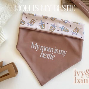 May include: A brown dog bandana with the text "My mom is my bestie" in white script. The top portion features a pattern of iced drinks and popsicles on a light pink background. The brand name "ivy & banks" is in the bottom right corner.