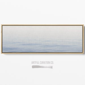 May include: A rectangular canvas print featuring a serene seascape with a gradient of blue hues. The artwork is framed in a natural wood tone, with the text "ARTFUL CURATION CO." at the bottom.