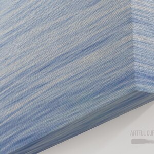 May include: A canvas art piece with a textured surface. The artwork features a diagonal pattern of light blue and white brushstrokes, creating a flowing, abstract design. The corner of the canvas is visible, showing the wrapped edges.