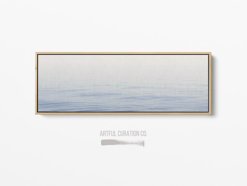 May include: A rectangular canvas print featuring a serene seascape with a gradient of blue hues. The artwork is framed in a natural wood tone, with the text "ARTFUL CURATION CO." at the bottom.