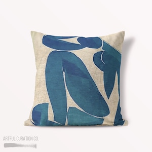 May include: A decorative throw pillow with a blue abstract design on a beige background. The design resembles a person sitting with their legs crossed.