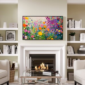 May include: A living room interior with a fireplace, two armchairs, a coffee table, and a bookshelf on each side of the fireplace. The fireplace has a white mantel and a black firebox with flames inside. Above the fireplace is a framed painting of a colorful field of flowers. The bookshelves are filled with books and decorative objects.