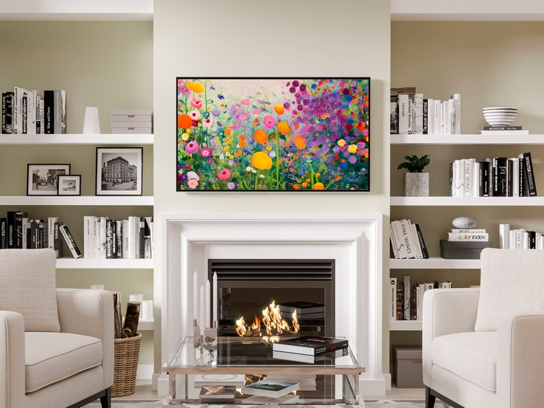 May include: A living room interior with a fireplace, two armchairs, a coffee table, and a bookshelf on each side of the fireplace. The fireplace has a white mantel and a black firebox with flames inside. Above the fireplace is a framed painting of a colorful field of flowers. The bookshelves are filled with books and decorative objects.