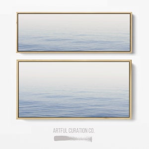 May include: Two framed wall art pieces featuring a serene ocean scene. The artwork depicts a gradient of blue and white, with subtle wave patterns. The frames are a natural wood color, adding a touch of warmth to the minimalist design.