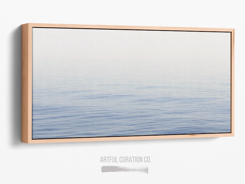 May include: A rectangular canvas print featuring a serene seascape. The artwork depicts a gradient of colors, transitioning from a light, misty sky to a calm, blue ocean. The canvas is framed in a natural wood border, adding a touch of warmth to the cool tones of the artwork.