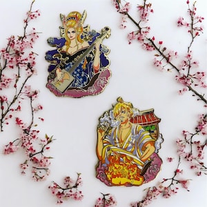 May include: Two enamel pins featuring anime characters. One pin depicts a woman playing a stringed instrument, the other a man cooking. Both pins have gold-colored borders and are surrounded by pink floral accents.