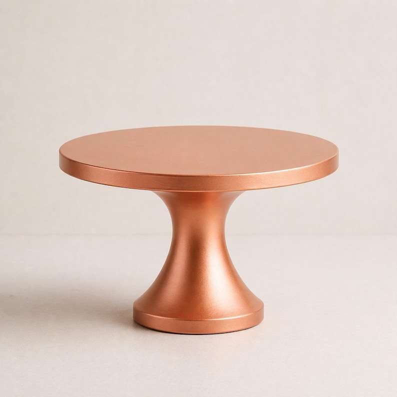 May include: A copper-colored cake stand with a round top and a pedestal base. The stand has a smooth, metallic finish and a classic design. Perfect for displaying cakes, cupcakes, or other desserts. The stand is approximately 10 inches in diameter.