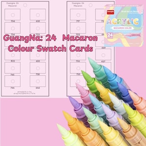 Puede incluir: Un conjunto de 24 marcadores acrílicos de colores pastel con puntas de pincel. Los marcadores están dispuestos en forma de abanico con las puntas hacia arriba. Los marcadores están etiquetados "GuangNa: 24 Macaron Colour Swatch Cards".