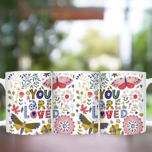 May include: Three white ceramic mugs with a floral pattern and the text "You are loved" in colorful letters. The mugs have a butterfly design and are perfect for a gift.