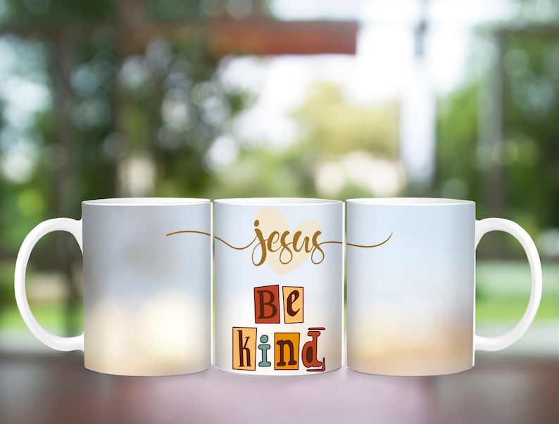 May include: Three white ceramic mugs with a blurred background. The middle mug has the words "Jesus Be Kind" in colorful block letters.