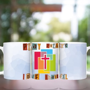 May include: Three white ceramic mugs with a colorful design featuring the words "Pray Forgive Love Thankful" and a cross in the center. The mugs are arranged in a row on a table.