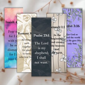 May include: A collection of five rectangular bookmarks with inspirational quotes from the Bible. Each bookmark features a different design, including floral patterns and watercolor backgrounds in shades of pink, purple, and beige. The text includes verses from Isaiah, Romans, Psalm, Genesis, and John.