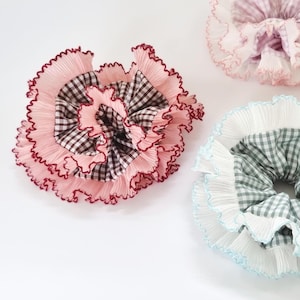 May include: Three hair scrunchies with ruffled fabric and gingham patterns. The scrunchies are in pink, blue, and green.