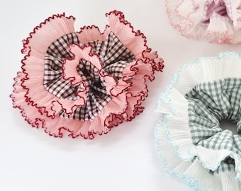 May include: Three hair scrunchies with ruffled fabric and gingham patterns. The scrunchies are in pink, blue, and green.