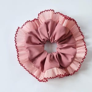 May include: A pink and light pink hair scrunchie with a ruffled edge and a burgundy trim.