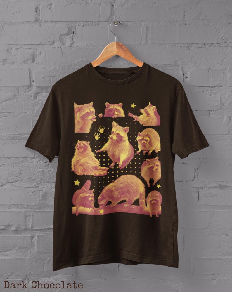 K&ouml;nnte beinhalten: Dunkel schokoladenfarbenes T-Shirt mit einer Collage von Waschb&auml;ren in verschiedenen Posen, mit einem gelb-rosa Farbschema. Das T-Shirt enth&auml;lt unten den Text "Dark Chocolate".