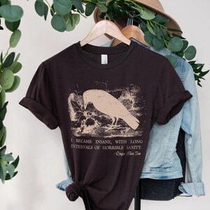 May include: A dark brown t-shirt with a vintage illustration of a raven and a quote from Edgar Allan Poe: "I became insane, with long intervals of horrible sanity."
