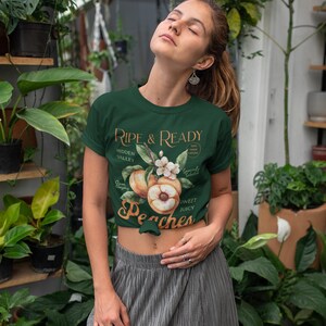 May include: Dark green t-shirt with the text "Ripe & Ready" and a peach graphic. The shirt features a crew neck and short sleeves. The design includes peaches, flowers, and the words "Hidden Valley" and "Sweet Juicy Peaches".