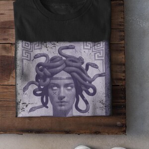 May include: Black t-shirt featuring a Medusa graphic. The design shows a detailed illustration of Medusa's face with snakes for hair, set against a faded, textured background. The word "Black" is printed at the bottom.