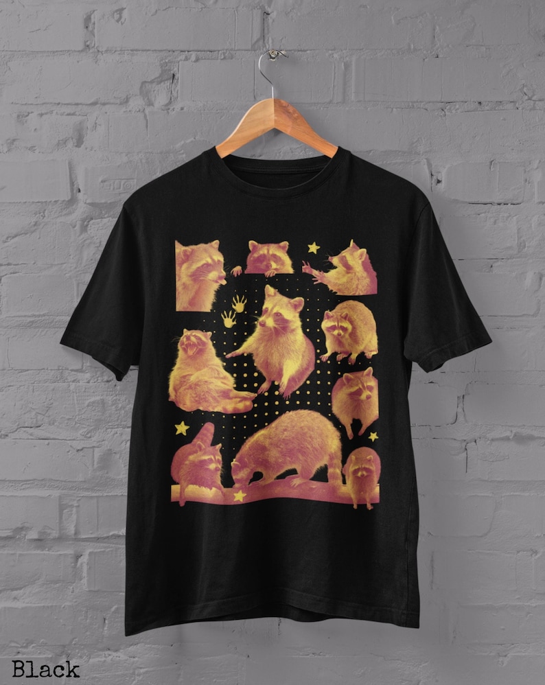 K&ouml;nnte beinhalten: Schwarzes T-Shirt mit einem Design von Waschb&auml;ren in verschiedenen Posen, mit gelben und roten Farbt&ouml;nen. Das Design enth&auml;lt Sterne und Handabdr&uuml;cke. Das Wort "Black" ist unten aufgedruckt.