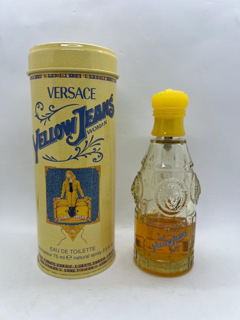May include: A yellow cylindrical tin and a perfume bottle. The tin reads "VERSACE Yellow Jeans Woman" with a blue denim-like background. The perfume bottle is clear with a yellow cap and contains a golden liquid. The bottle has the words "Yellow Jeans" in blue.
