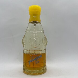 May include: A clear glass perfume bottle with a yellow cap. The bottle has a rectangular shape with embossed details and contains a golden-coloured liquid. The words "Yellow Jeans" are printed in blue on the front.