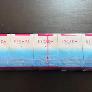 May include: A row of five Escada Into The Blue eau de parfum sample vials in white and blue gradient packaging with pink accents. Each rectangular box features the text Escada Into The Blue and indicates a volume of 2 ml / 0.06 fl oz.