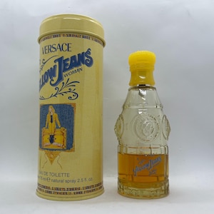 May include: Versace Yellow Jeans Woman eau de toilette, presented in a bottle with a yellow cap and a cylindrical container. The container displays the Versace logo and a denim-themed illustration. The bottle contains 75 ml of perfume.
