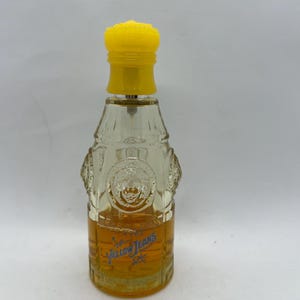 May include: A clear glass perfume bottle with a yellow cap. The bottle has a textured design and contains a golden-coloured liquid. The words "Yellow Jeans" are printed on the front of the bottle.