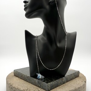 May include: A pair of clear, translucent earplugs with blue accents connected by a thin, silver-toned metal chain. The earplugs are designed to be worn in the ears, with the chain draping down from the ear to connect the two pieces together.