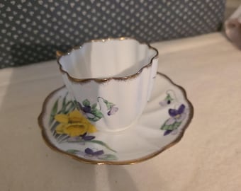Taza y platillo de porcelana fina vintage Royal Bone China con diseño floral de violetas y narcisos, ribete dorado.