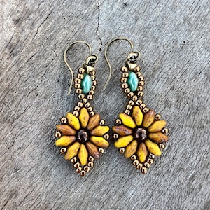 May include: A pair of dangle earrings with a sunflower design. The earrings are made with brown and yellow beads and have a green bead at the top.
