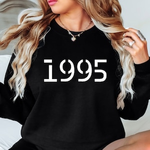 Op de afbeelding: Zwart sweatshirt met witte tekst die "1995" zegt.