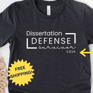 May include: A dark gray t-shirt with the text "Dissertation Defense Survivor 6.21.24" printed on the front. The shirt is available with an option to add a date. Free shipping is offered.