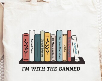 May include: A white tote bag with a graphic of a bookshelf with several books. The books have titles including "Animal Farm", "Song of Solomon", "Of Mice and Men", "The Sun Also Rises", "Lolita", and "The Color Purple". The text "I'M WITH THE BANNED" is printed below the bookshelf.