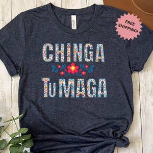 May include: A dark blue t-shirt with the text "CHINGA TUMADA" in colorful embroidered letters. The letters are surrounded by colorful flowers.