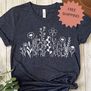 May include: A dark gray t-shirt with a white design of stylized flowers and leaves. The design includes the text "It's true, I'm pretty."