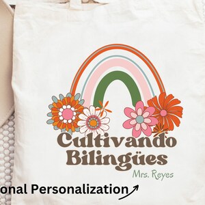Op de afbeelding: Een witte tote bag met een regenboog, bloemen en de tekst "Cultivando Bil&iacute;ng&uuml;es" in bruine letters. De tekst "Mrs. Reyes" staat in kleinere bruine letters onder de hoofdtekst.
